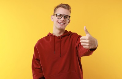 Photo of Happy man showing thumbs up on yellow background. Like gesture