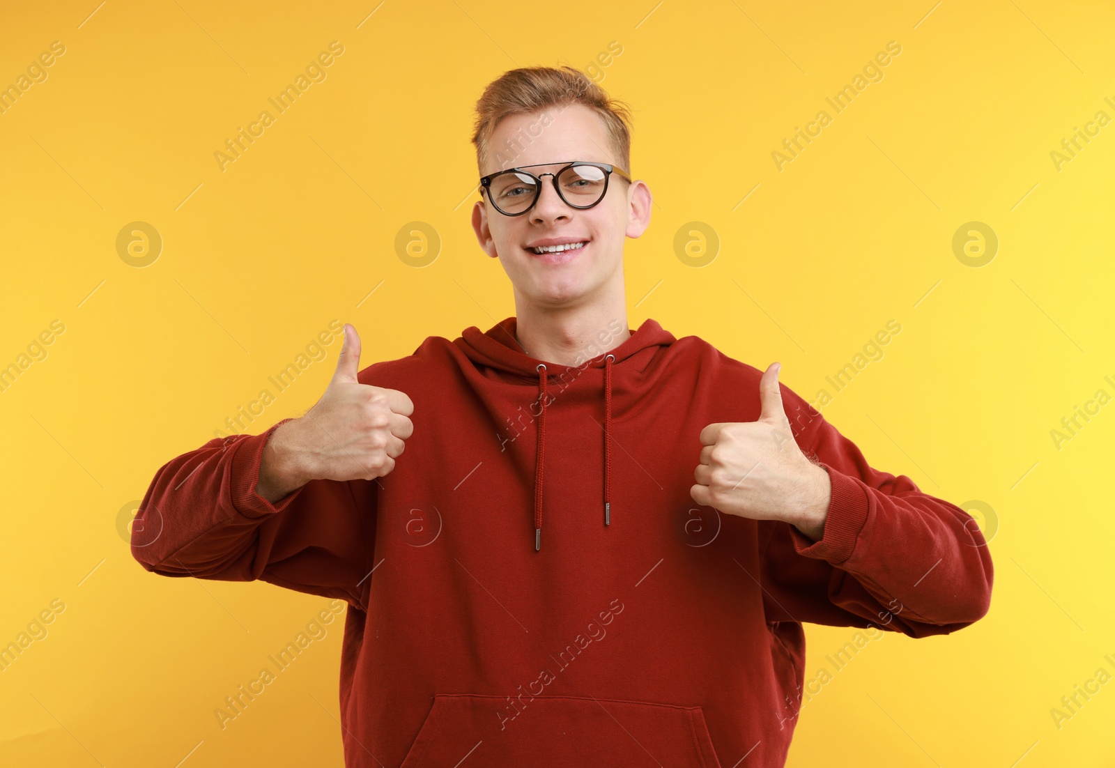 Photo of Happy man showing thumbs up on yellow background. Like gesture