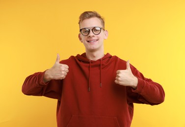 Photo of Happy man showing thumbs up on yellow background. Like gesture