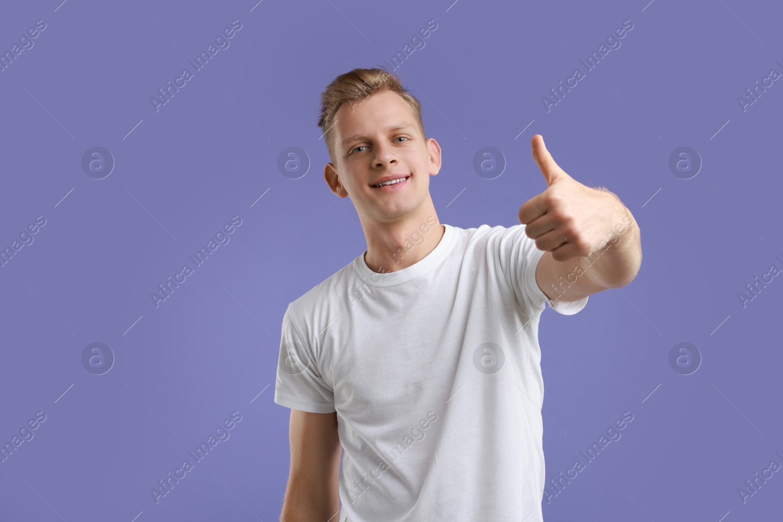 Photo of Happy man showing thumbs up on purple background. Like gesture