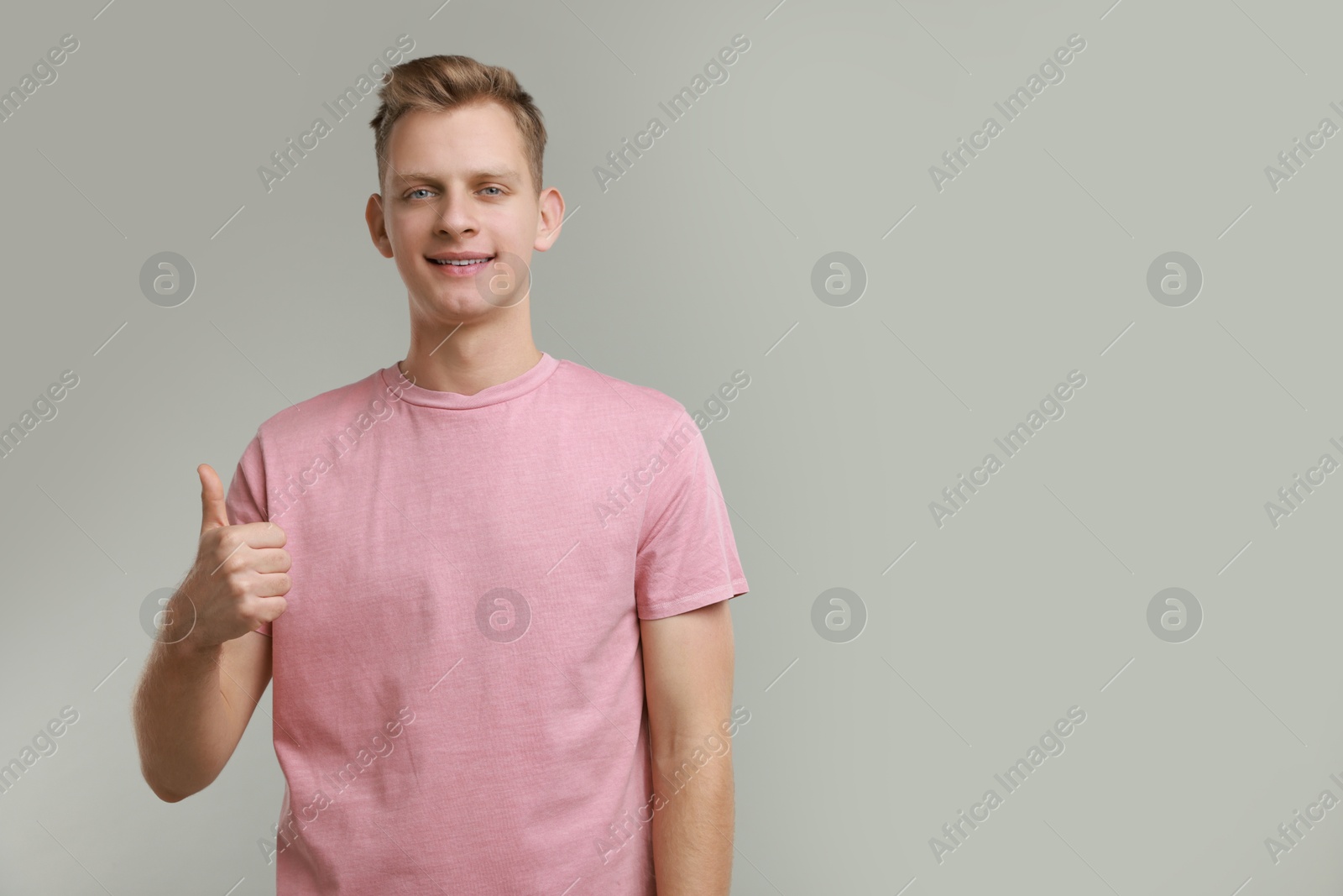 Photo of Happy man showing thumbs up on grey background, space for text. Like gesture