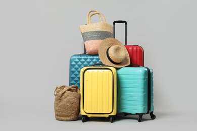 Photo of Many colorful suitcases, beach bags and straw hat on grey background