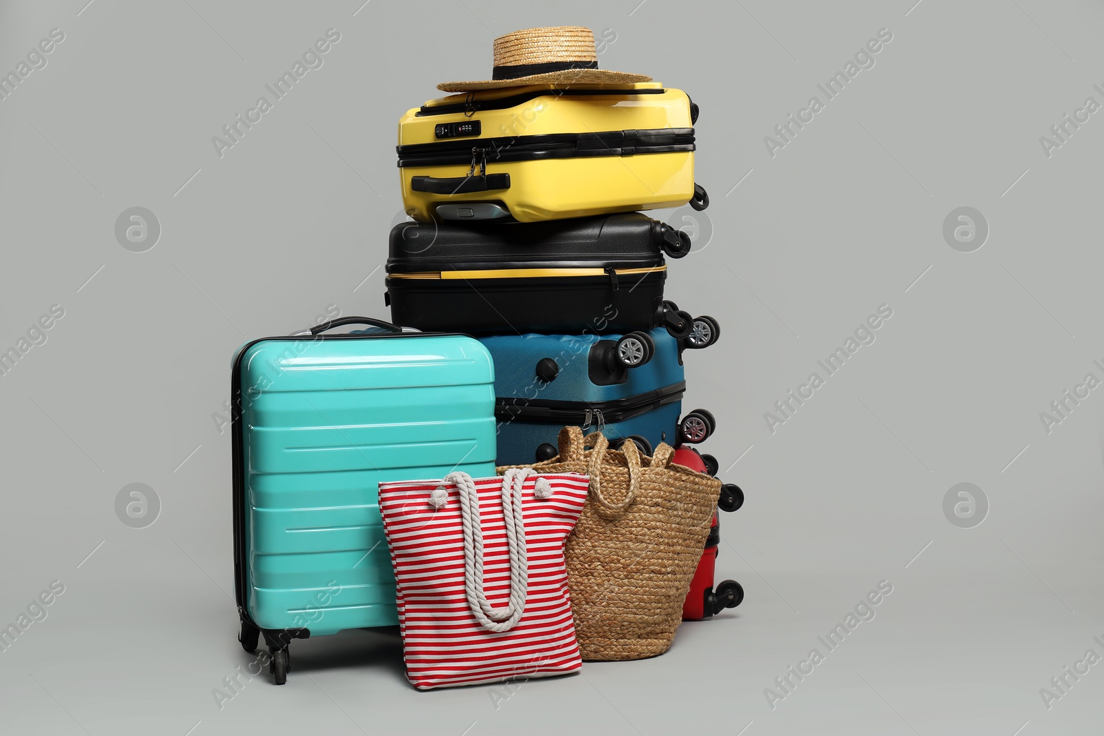 Photo of Stack of colorful suitcases, beach bags and straw hat on grey background