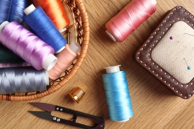 Photo of Sewing threads, snips, pincushion and thimble on wooden table, flat lay