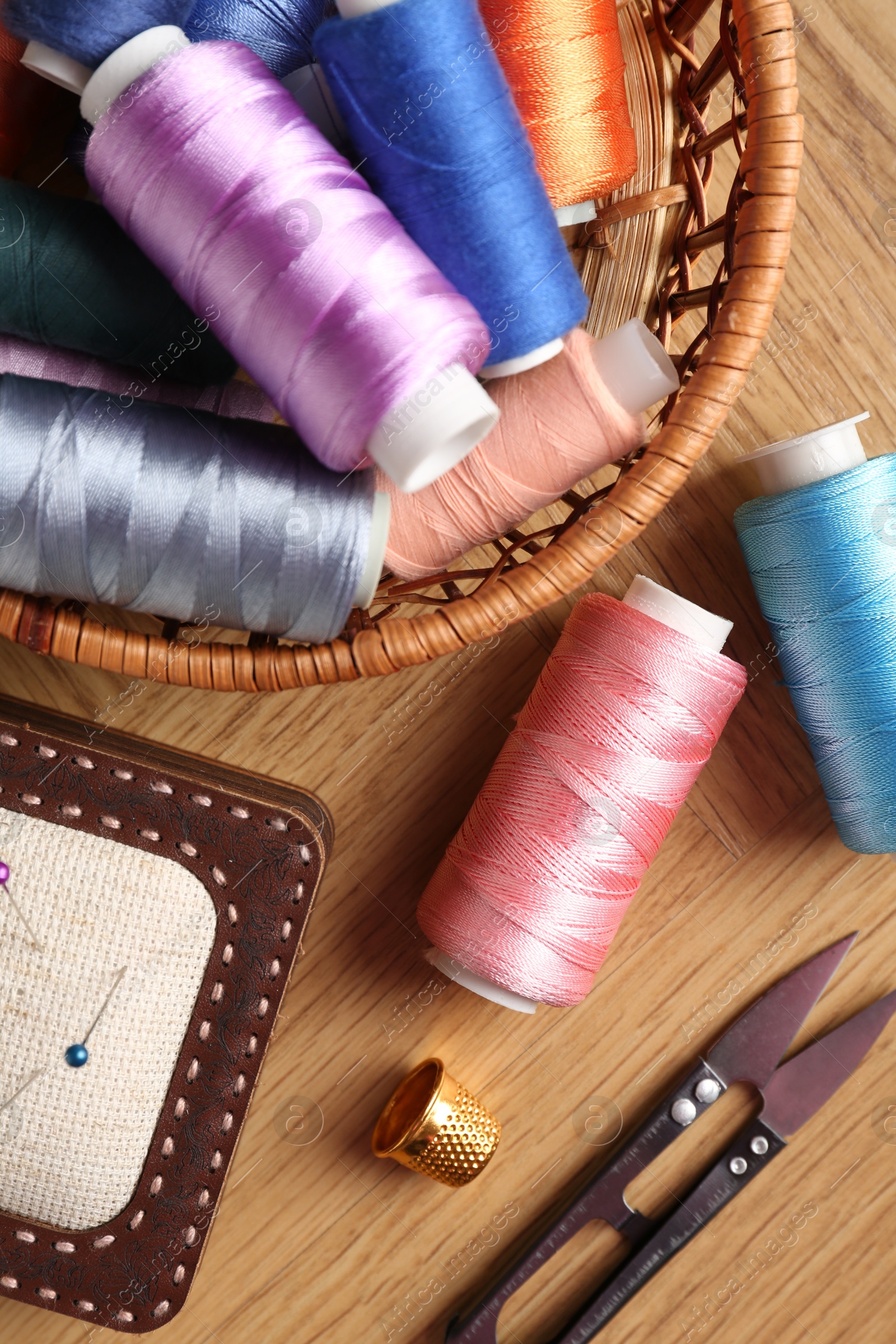 Photo of Sewing threads, snips, pincushion and thimble on wooden table, flat lay