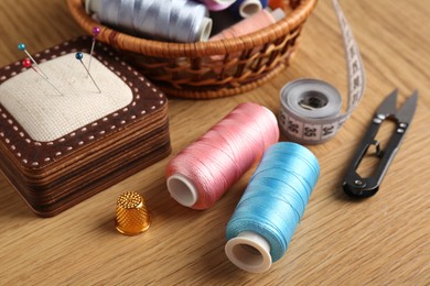 Photo of Sewing threads, snips, pincushion and thimble on wooden table, closeup