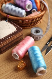 Photo of Sewing threads, pincushion and thimble on wooden table, closeup