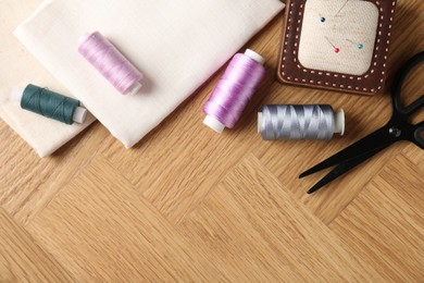 Photo of Sewing threads and other supplies on wooden table, flat lay. Space for text