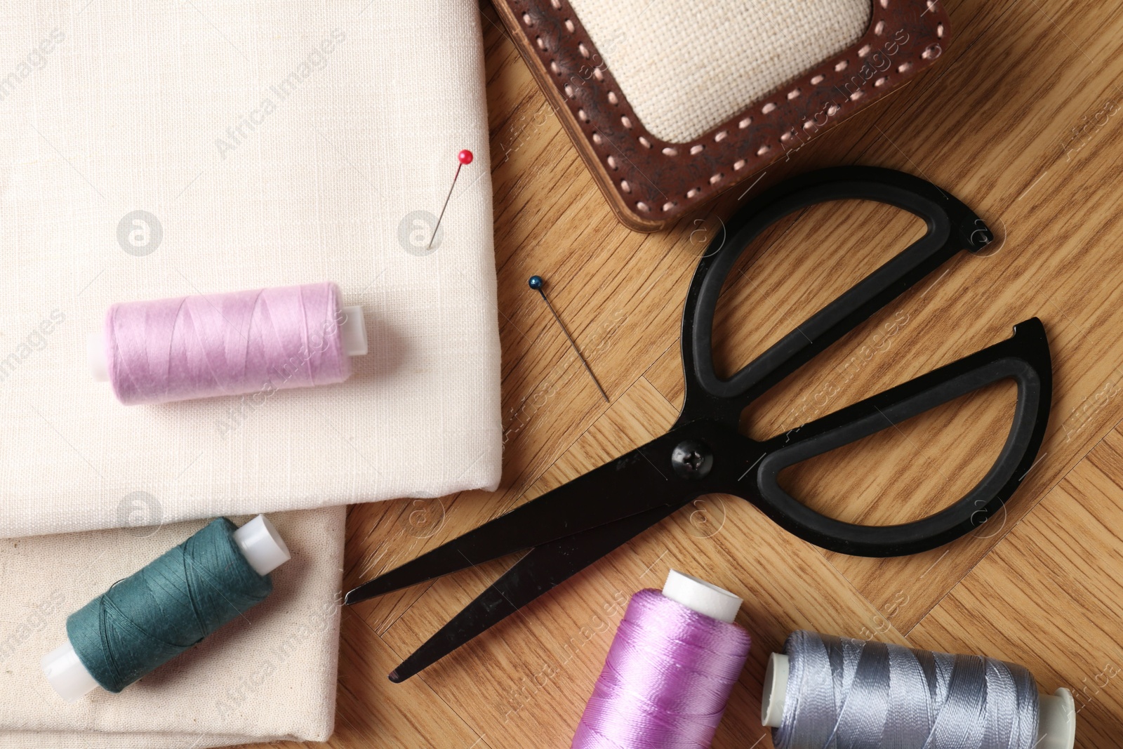 Photo of Sewing threads and other supplies on wooden table, flat lay