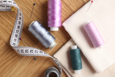 Photo of Sewing threads and other supplies on wooden table, flat lay