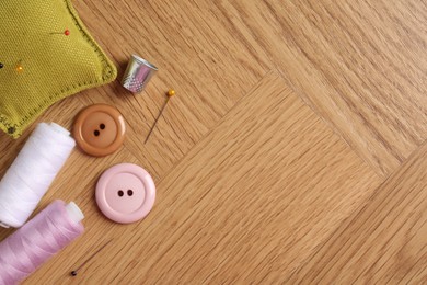 Photo of Sewing threads and other supplies on wooden table, flat lay. Space for text