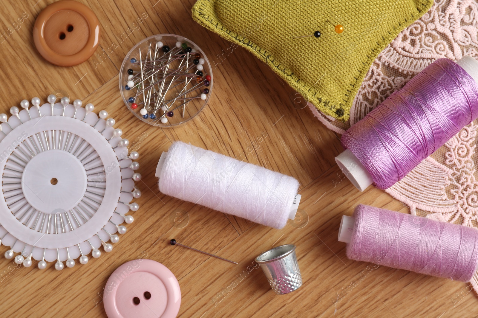 Photo of Sewing threads and other supplies on wooden table, flat lay