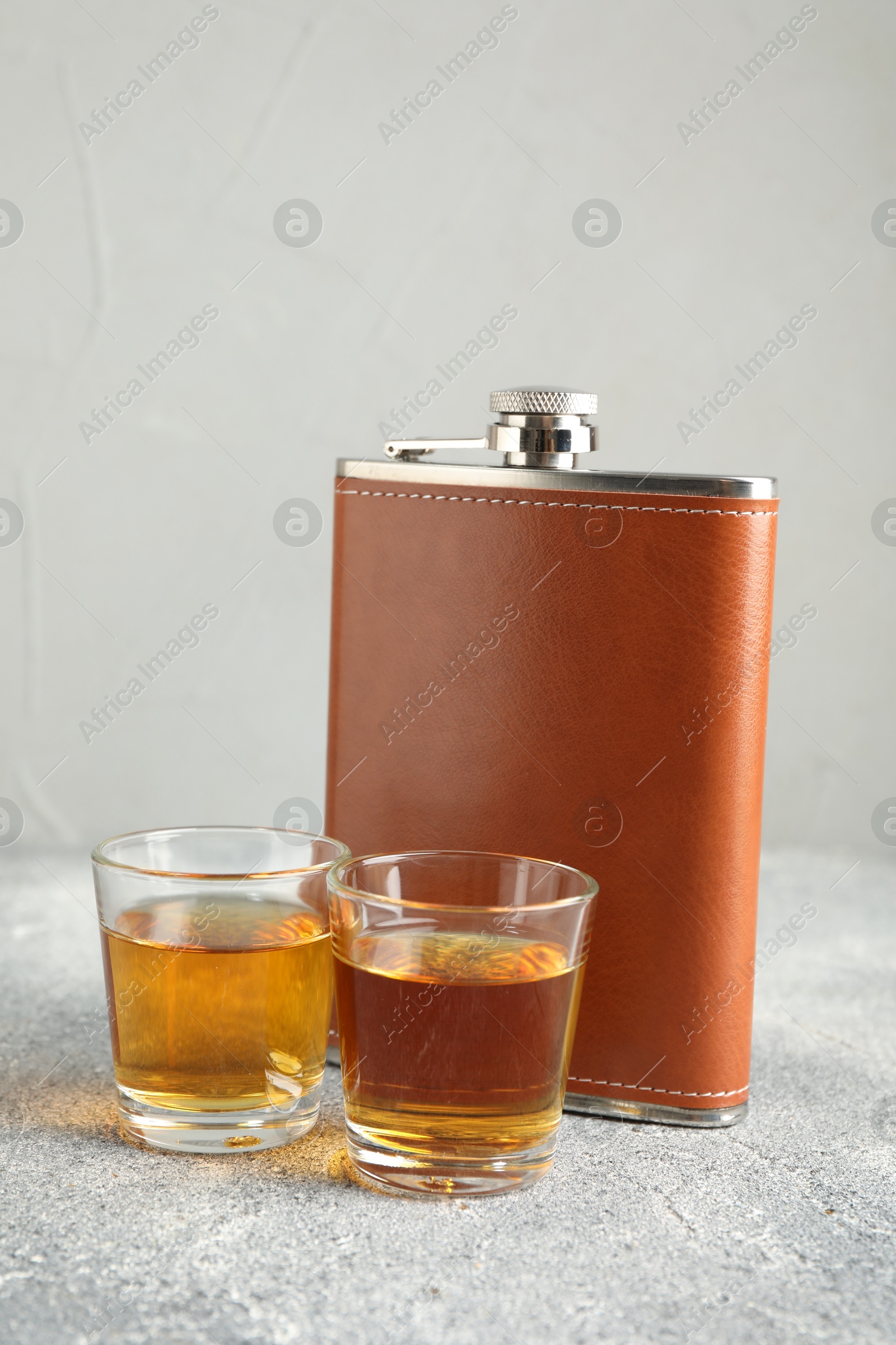 Photo of Hip flask and glasses with whiskey on grey table