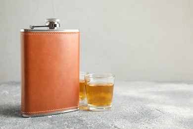 Photo of Hip flask and glasses with whiskey on grey table. Space for text