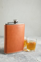 Photo of Hip flask and glasses with whiskey on grey table