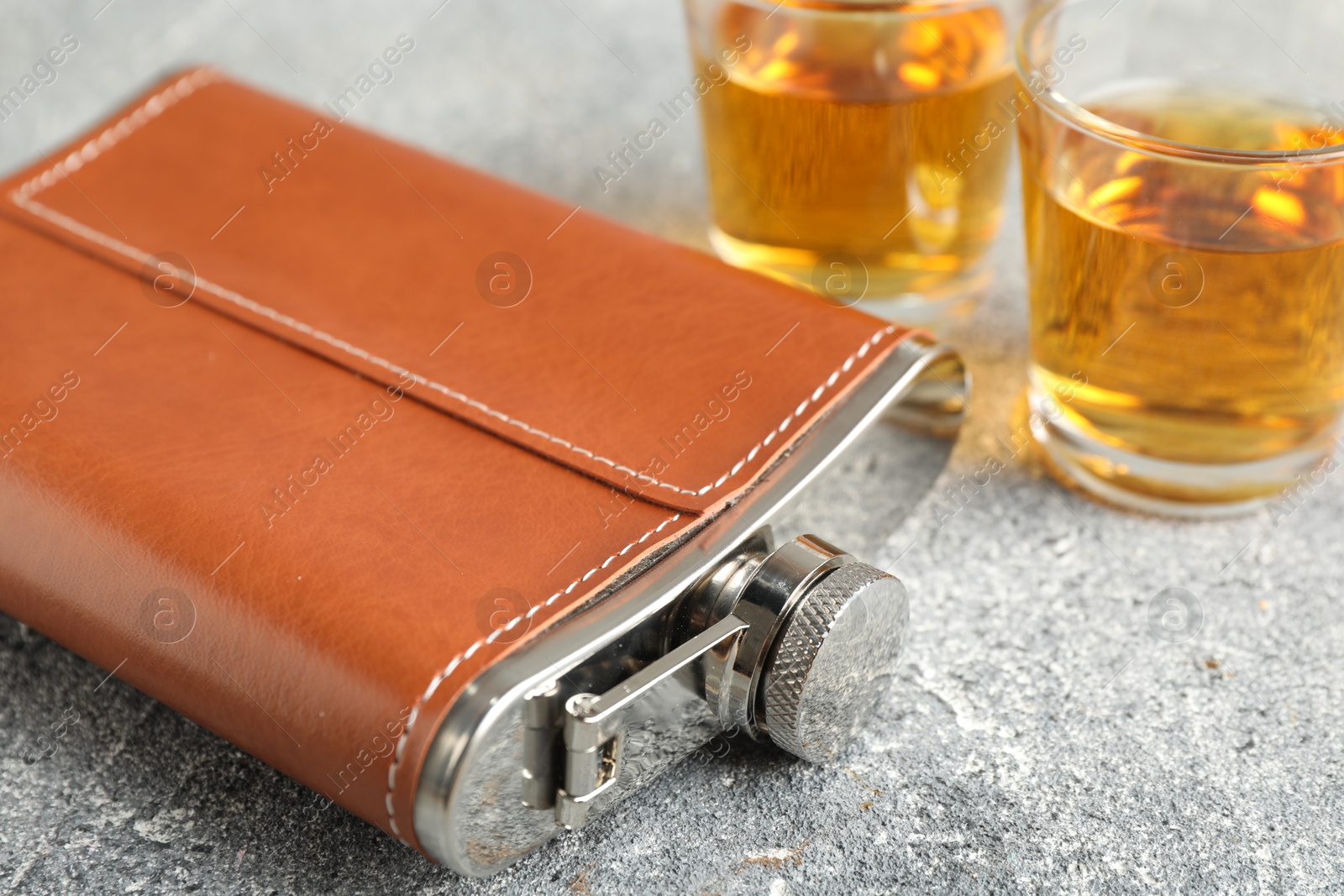 Photo of Hip flask and glasses with whiskey on grey table, closeup