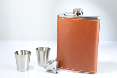 Photo of Hip flask, funnel and cups on white table