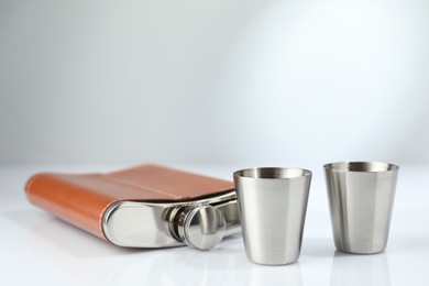 Photo of Hip flask and cups on white table. Space for text