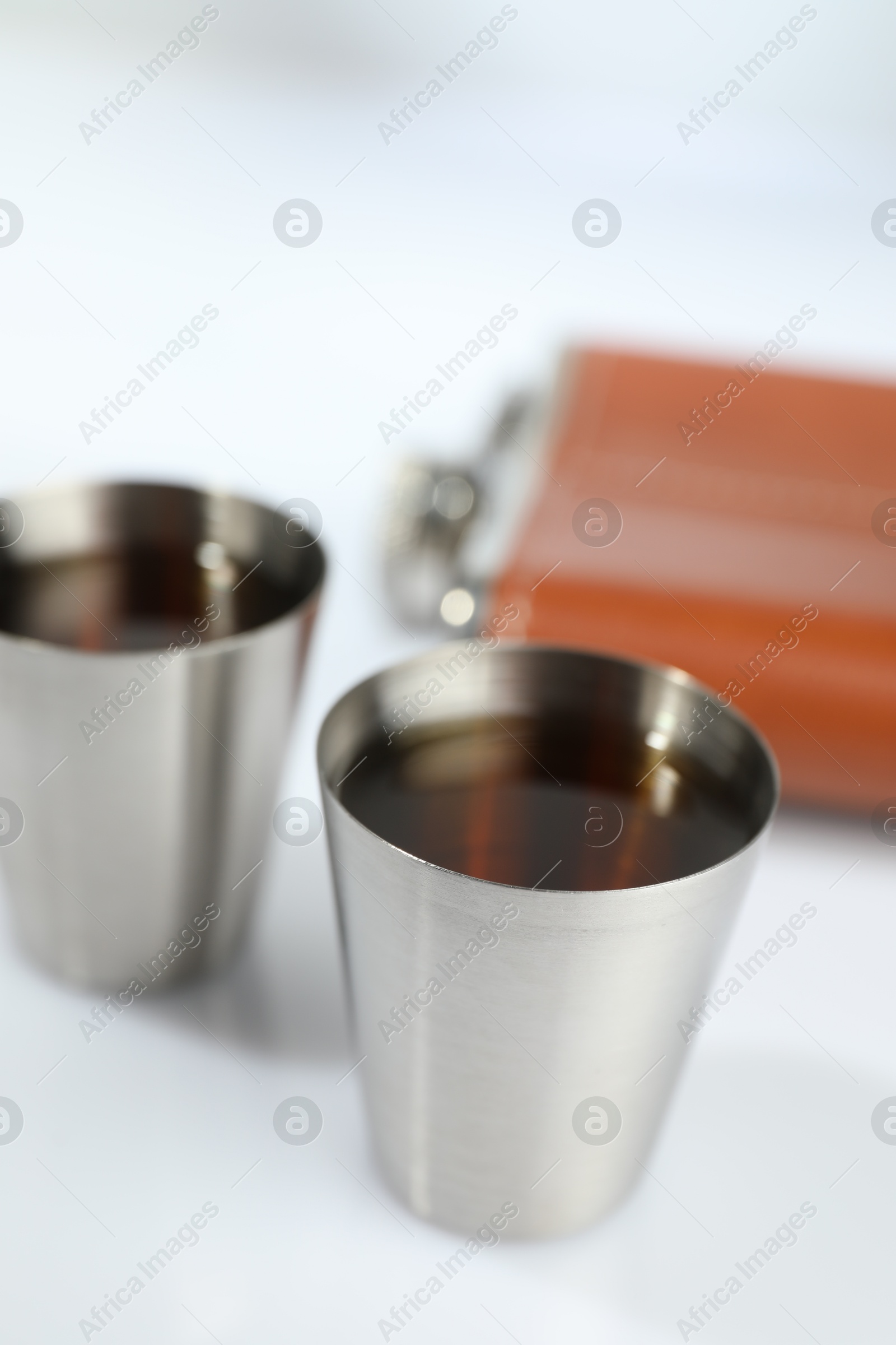 Photo of Hip flask and cups with whiskey on white table, closeup