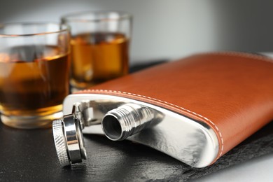 Photo of Hip flask and glasses of whiskey on table, selective focus