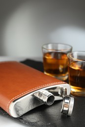 Photo of Hip flask and glasses of whiskey on table, selective focus