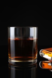 Photo of Hip flask and glass of whiskey on black mirror surface, closeup