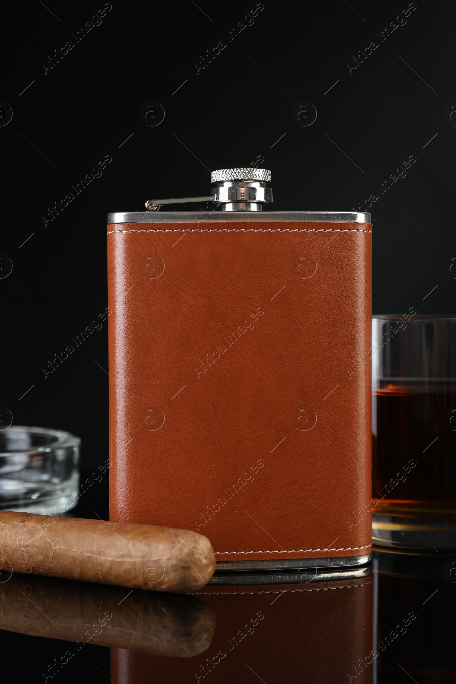 Photo of Hip flask, glass of whiskey, cigar and ashtray on black mirror surface