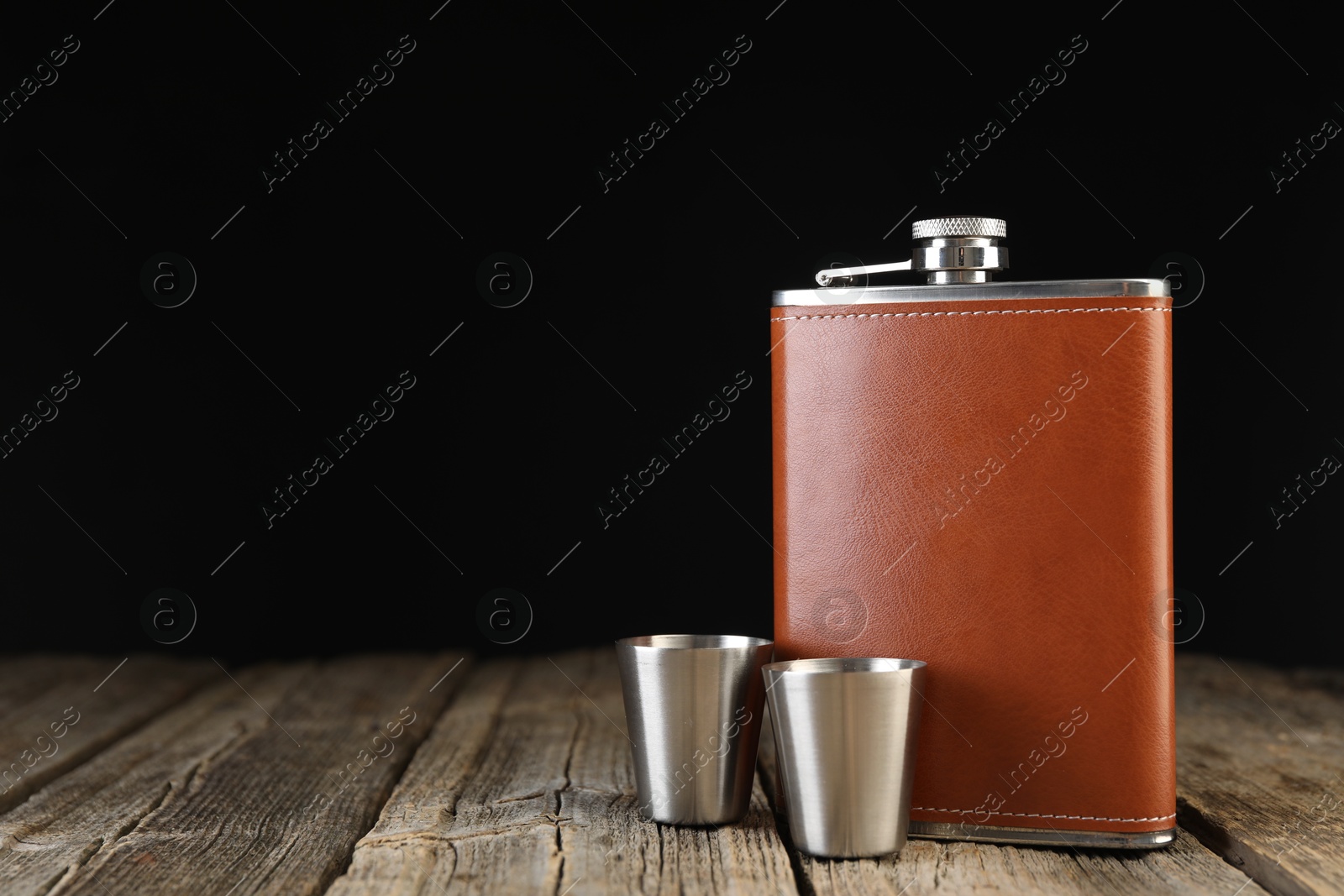 Photo of Hip flask and cups on wooden table. Space for text