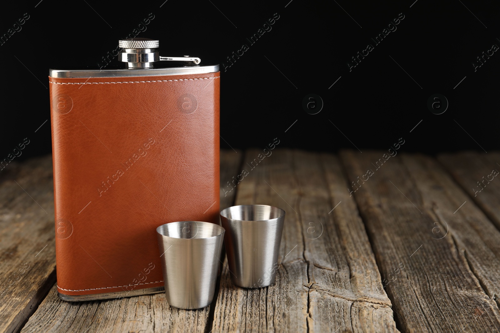 Photo of Hip flask and cups on wooden table. Space for text