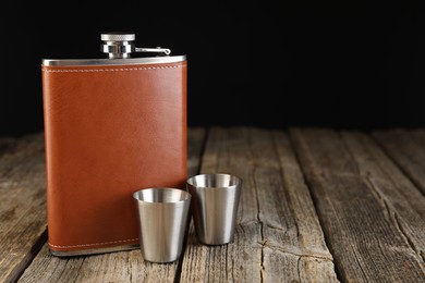 Photo of Hip flask and cups on wooden table. Space for text