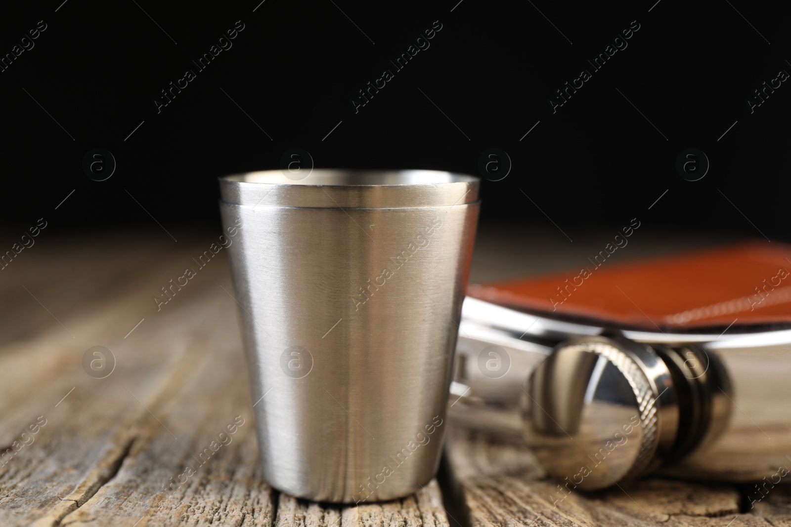 Photo of Hip flask and cups on wooden table, closeup