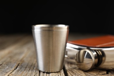 Photo of Hip flask and cups on wooden table, closeup