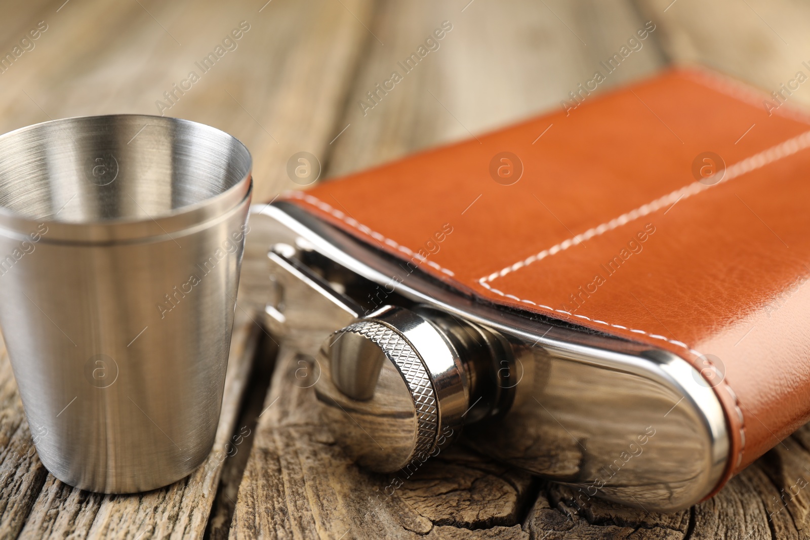 Photo of Hip flask and cups on wooden table, closeup