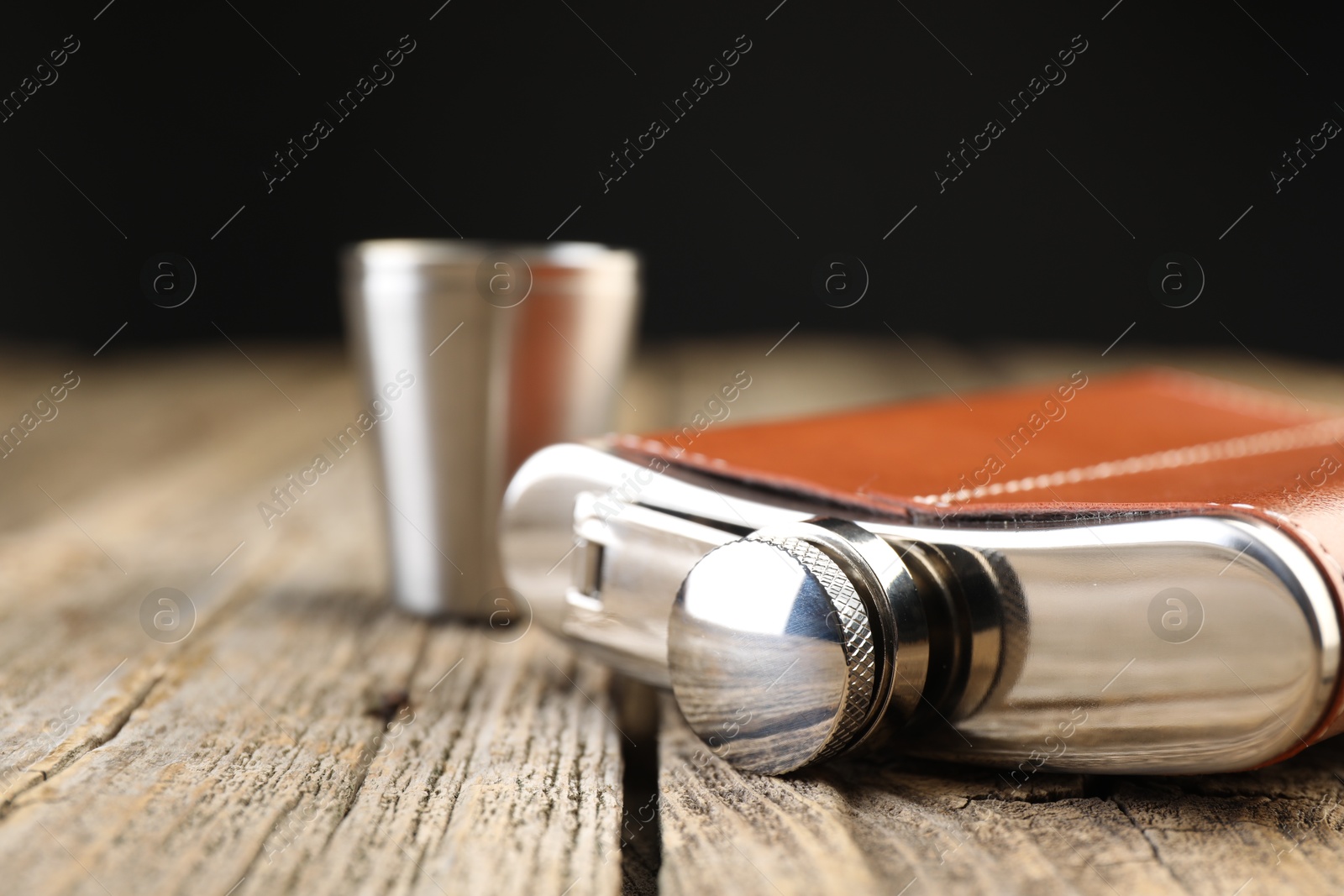 Photo of Hip flask and cups on wooden table, closeup