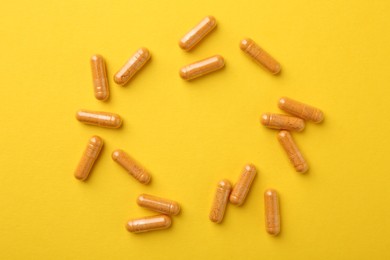 Photo of Turmeric capsules on yellow background, flat lay. Space for text