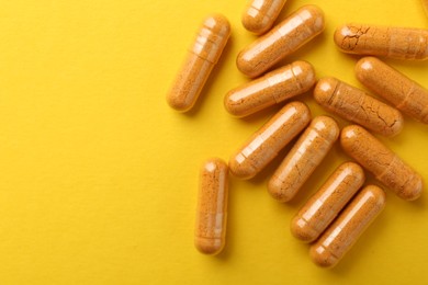 Photo of Turmeric capsules on yellow background, flat lay. Space for text