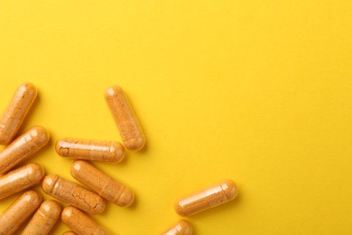 Photo of Turmeric capsules on yellow background, flat lay. Space for text