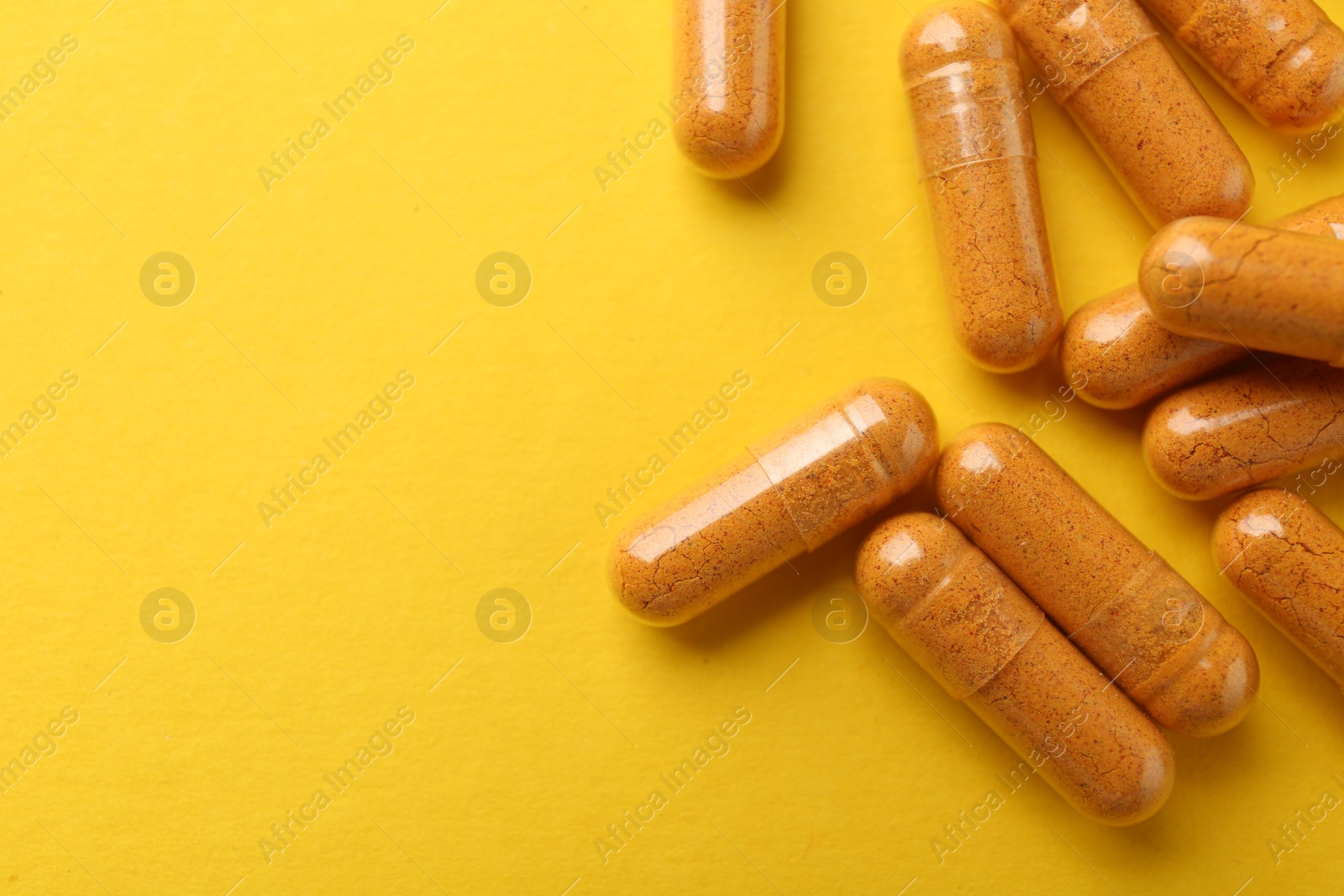 Photo of Many turmeric capsules on yellow background, flat lay. Space for text