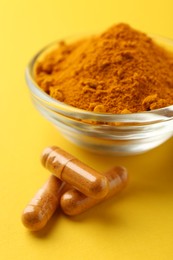 Photo of Turmeric powder in bowl and capsules on yellow background, closeup