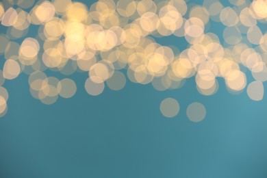 Photo of Blurred view of golden lights on light blue background. Bokeh effect