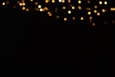 Photo of Blurred view of golden lights on black background, space for text. Bokeh effect