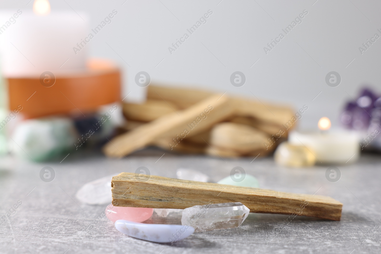 Photo of Palo santo sticks, gemstones and burning candles on light grey table, closeup