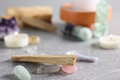 Photo of Palo santo sticks, gemstones and burning candles on light grey table, closeup