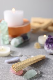 Photo of Palo santo sticks, gemstones and burning candles on light grey table, closeup