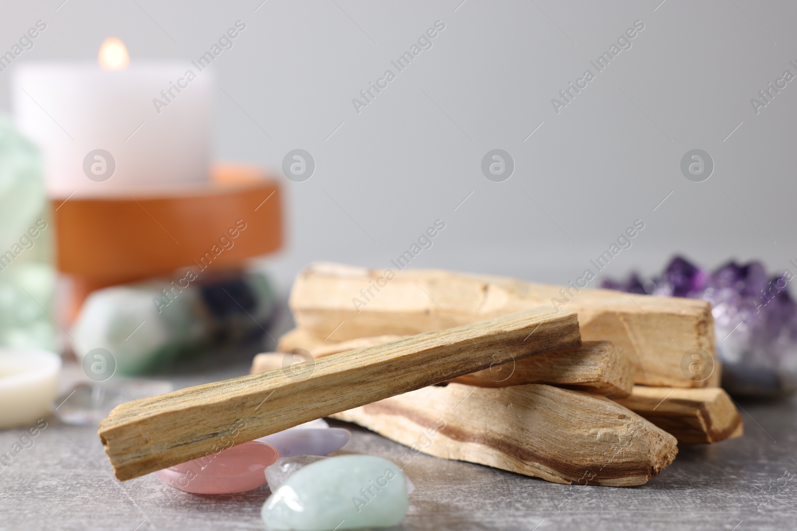 Photo of Palo santo sticks, gemstones and burning candle on light grey table, closeup