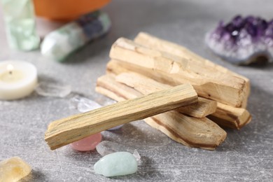 Photo of Palo santo sticks, gemstones and burning candle on light grey table, closeup