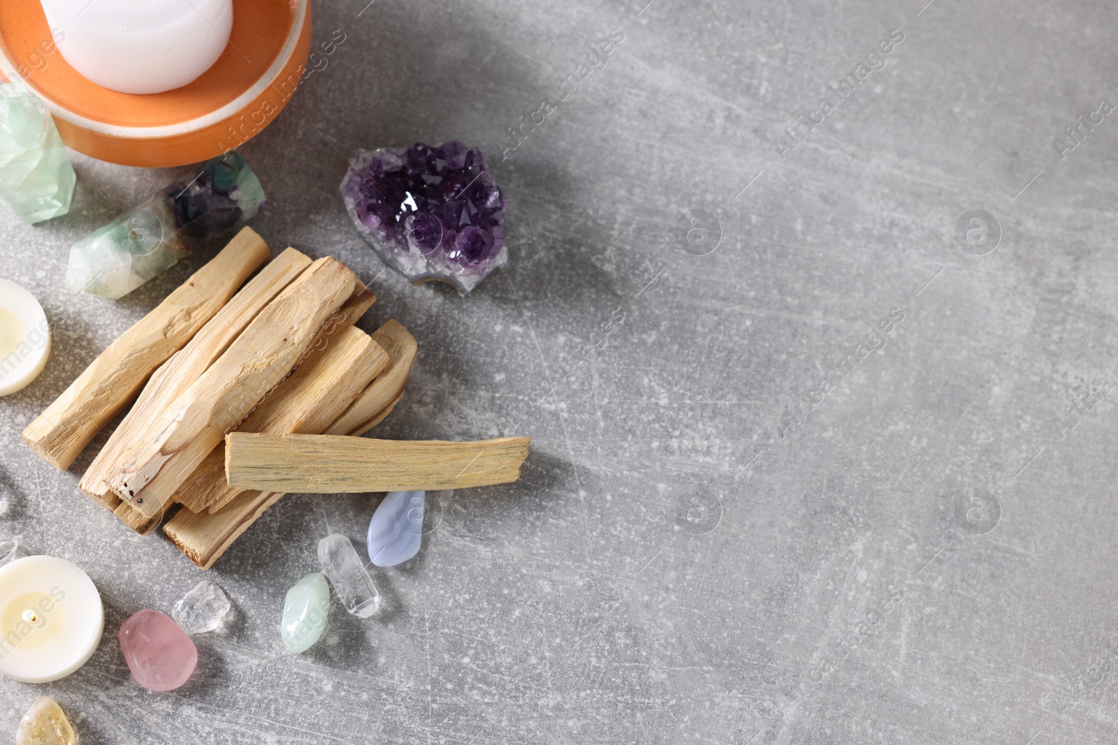 Photo of Palo santo sticks, gemstones and burning candles on light grey table, flat lay. Space for text