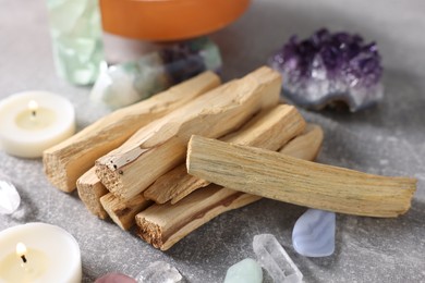 Photo of Palo santo sticks, gemstones and burning candles on light grey table, closeup