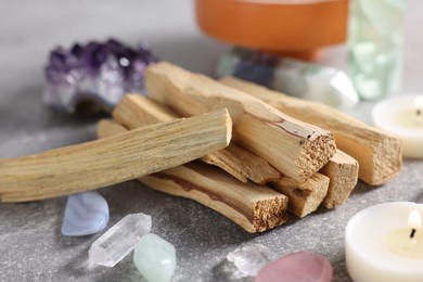 Photo of Palo santo sticks, gemstones and burning candles on light grey table, closeup