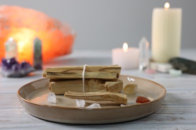 Photo of Palo santo sticks, gemstones and burning candles on white wooden table, closeup